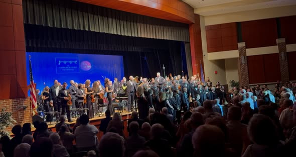 Symphony concert recital hall conclusion. Orchestra and chorus members are standing while the audience is applauding.